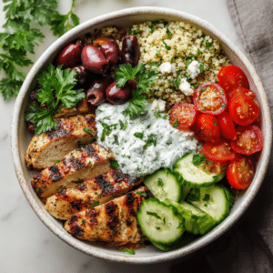 Overhead view of a colorful Mediterranean chicken bowl with quinoa, vegetables, and creamy tzatziki.